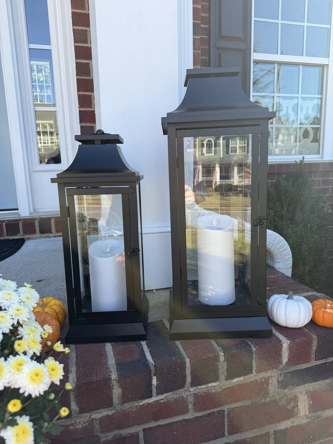 Two refreshed black lanterns with white flameless candles on a brick porch
