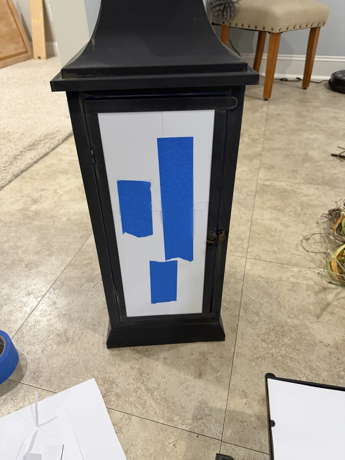 White printer paper and blue painter's tape protecting the glass of a lantern before painting